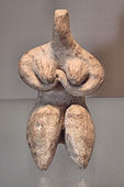 Stylized seated female figure with arms folded under her breasts