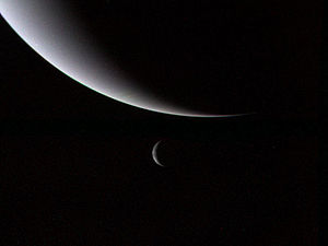 Two large partially illuminated spherical bodies: a large one at the top and a small one below it. The light is coming from the left making the bodies look like the waxing crescent moon.