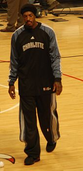 A man, wearing black pants and a black shirt with the word «CHARLOTTE» on the front, is walking on a basketball court.