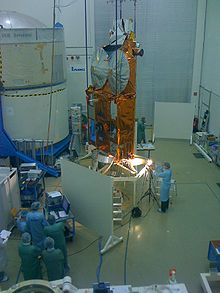Группа людей смотрит на космический аппарат обёрнутый в фольгу золотистого цвета установленный в центре зала